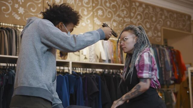 African-American criminal in clothing store aiming to the assistant with gun. Realtime