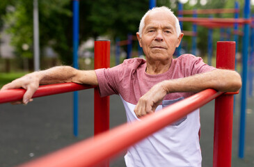 Obraz premium Senior sporty man performs various exercises on uneven bars in park