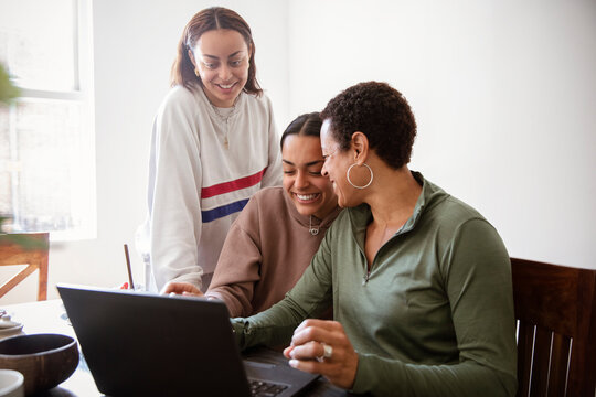 Happy mother and young adult daughters using laptop at home