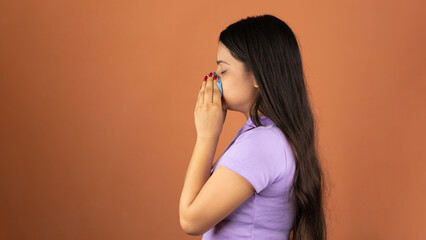 Young woman sneezing into a handkerchief because of her allergy or cold, isolated over color background