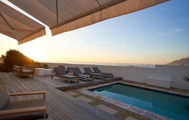 Lounge chairs along swimming pool on patio with ocean view