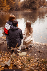 happy family with a child on an autumn walk in a city park with a lake, feeding ducks back view