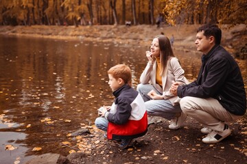 happy family with a child on an autumn walk in a city park with a lake, feeding ducks, family fun