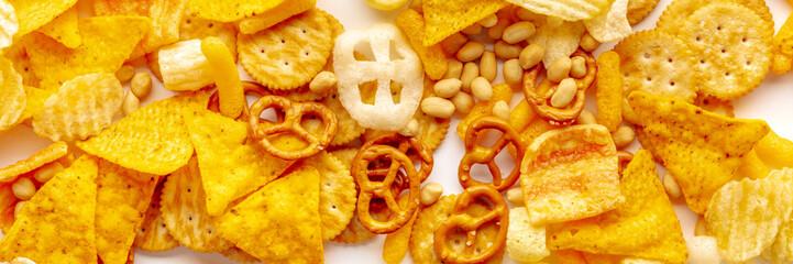 Salty snacks on a white table panorama. Party food banner. Potato and tortilla chips, salt crackers and other appetizers, shot from above - obrazy, fototapety, plakaty