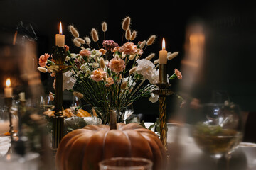 Decoration and serving of the festive table with autumn decor, candles and flowers and pumpkins and dishes.