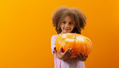 A modest Black girl carries a pumpkin in her hands as a decoration for the Halloween or Thanksgiving holiday.