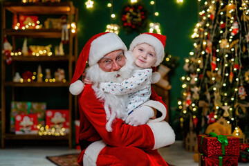 Fototapeta na wymiar Happy little boy in Santa's hat hugging with Santa Claus near Christmas tree. New Year concept 