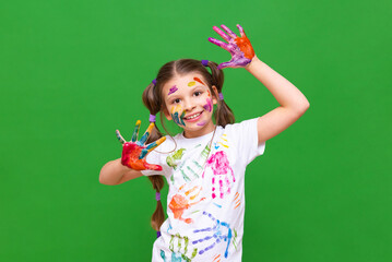 A little joyful girl with stained hands in paint makes faces and smiles, a little girl got dirty in...