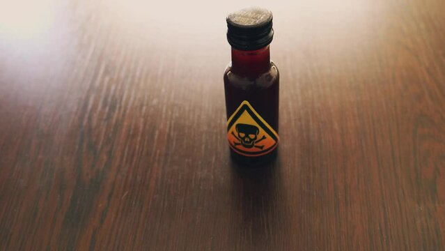 hand leaving a small bottle shaped poison pot on a wooden table,  with a yellow toxic sign represented by a skull icon in a yellow triangle - lethal concoction for a poisoning