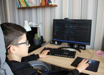 Boy teenager programmer sits at the computer and writes code, studies, works, hobby