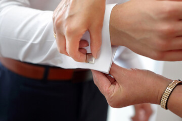 The cufflink for the shirt is put on by a mother for her son on his wedding day