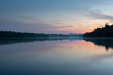 Landscape of river with fog on water surface and distant mountain at twilight, symmetric reflection and pastel colors