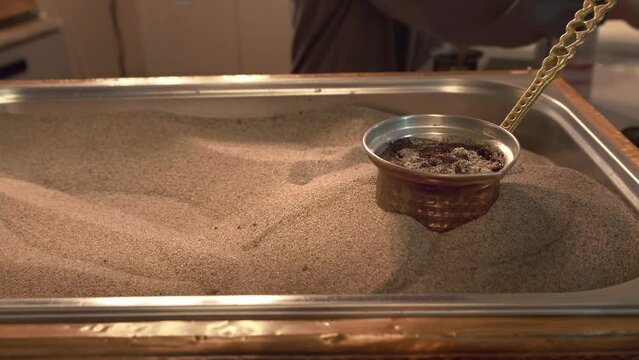 Traditional Turkish coffee preparation on hot sand. Copper cezve immersed in sand until liquid boils.