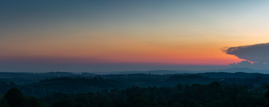 Glow in sky at twilight above hilly rural landscape in haze, hill layers in haze and vibrant glowing sky above horizon