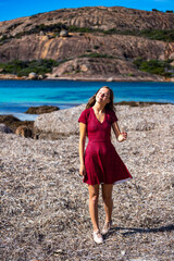 a long-haired girl in a dress walks on a paradise beach in western australia; a beach with turquoise water, white sand and massive mountains in the background