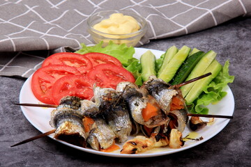 fried herring rolls stuffed with cheese on a bamboo skewer, served with tomatoes and cucumbers