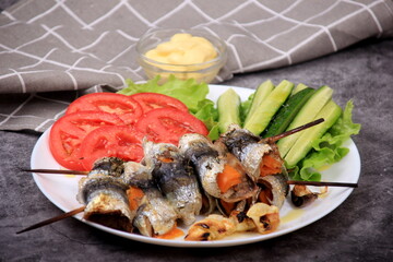 fried herring rolls stuffed with cheese on a bamboo skewer, served with tomatoes and cucumbers
