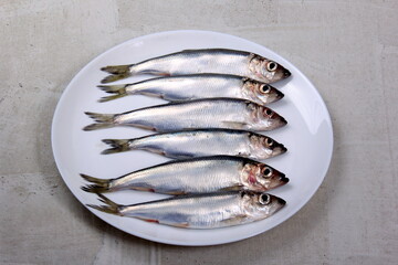 Several small silver fish, herrings with heads together on a white plate