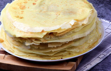 A stack of round thin pancakes on a wooden kitchen board