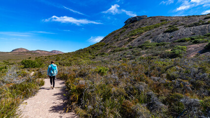 Obraz premium brave backpacker girl descends from frenchman peak in cape le grand national park in western australia, hiking and climbing a mountain with a backpack