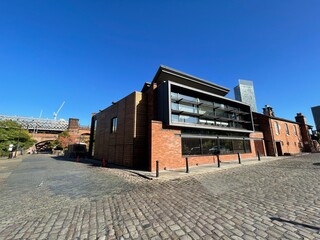 Modern building on an old cobblestone road with a clear blue sky background. Taken in Manchester England. 