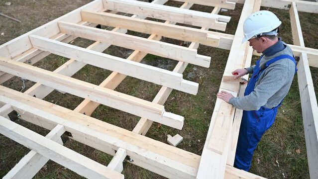 Man worker building wooden frame house on pile foundation. Carpenter measuring wooden planks. Carpentry concept.