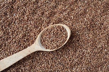 On the table is a wooden spoon with buckwheat grains. Around it are buckwheat grains.