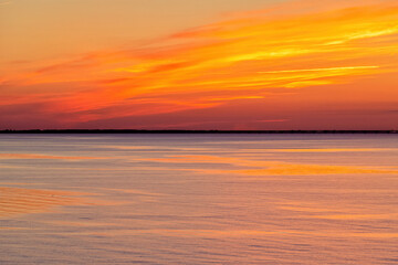 Bright twilight sunset sky over the sea. Wonderful sky after sunset in orange shades. The natural background. Purple hue of the sea and sky. Abstract lines of fire clouds.