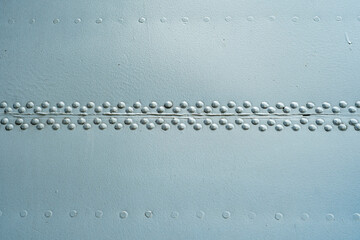 A close-up of a metal surface with heavy-duty rivets covered in silver paint.