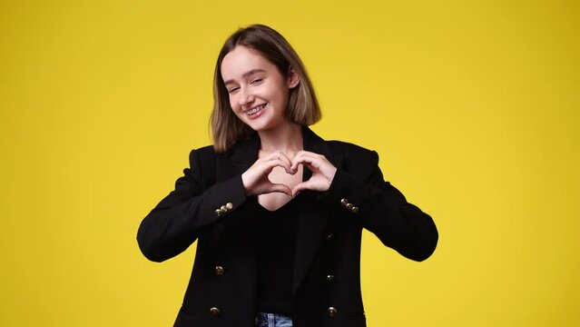 4k video of smiling female showing heart shape isolated over yellow background.