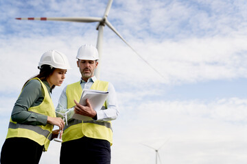 Two caucasian engineers standing on wind turbine field and discussing over documents