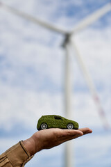 Unrecognizable hand holding green car model and wind turbine in the background