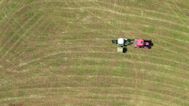 Aerial Birds Eye View Of Tractor Pulling Wrapped Hay Bale Across Green Field In Chmielno. Tracking Shot