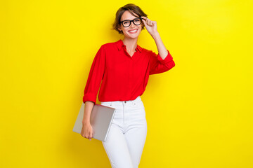 Portrait of gorgeous pretty positive girl with bob hairdo wear red shirt hold laptop touching glasses isolated on yellow color background