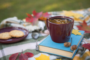Cup of black coffee standing on a blue book. Coffee on autumn day on the table, autumn atmosphere in the park or garden.
