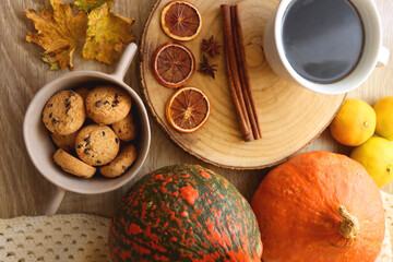 Cup of tea or coffee, seasonal spices, bowl of cookies, blanket, pumpkins, colorful leaves, books and tangerines on wooden table. Cozy hygge at home. Top view.