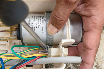 An electrician dismantles the control panel of a window type air conditioner control panel outside.