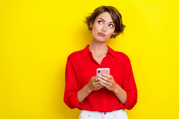 Fototapeta premium Portrait of positive thoughtful girl with bob hairstyle wear red shirt writing post in social media isolated on yellow color background
