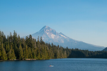 Mt Hood rises in the distance over Lost Lake in Oregon mid-afternoon.  The blue lake and green pine trees from the majestic mountain. 