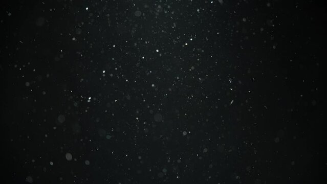 White dust particles flowing in the air on black background. Slow motion. 