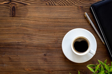Office table with cup of hot black coffee and notebook