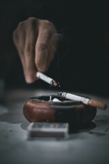 Vertical shot of a hand in a dark background flicking cigarette ash into an ashtray.