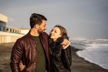 Beautiful couple in relationship hugging and loving each other at the first dating - Girl and boy enjoying the outdoor leisure activity at the romantic beach in autumn season - Couple relationship