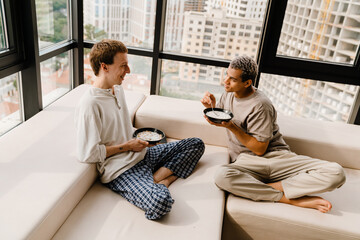 Happy multiracial gay couple talking while having breakfast at home