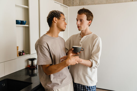 Happy Young Gay Couple Hugging While Drinking Coffee Together At Home