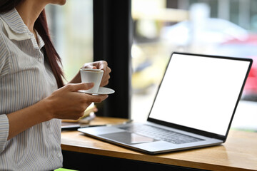 Selective focus on businesswoman's hands holding a espresso shot and looking to screen of laptop, Empty screen of laptop.