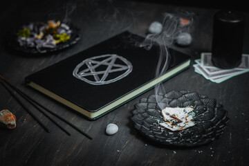 A black metal saucer with burnt paper, a leather book with a magic sign, ritual stones and a candle...