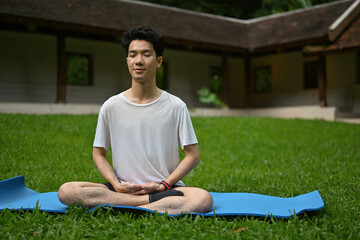 Portrait of Millennial man practicing and sitting in lotus asana pose on the grass field.