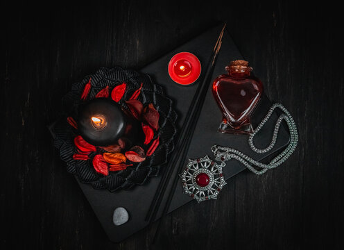 Black leather book, candle, red potion, amulet and ritual sticks on a black background.