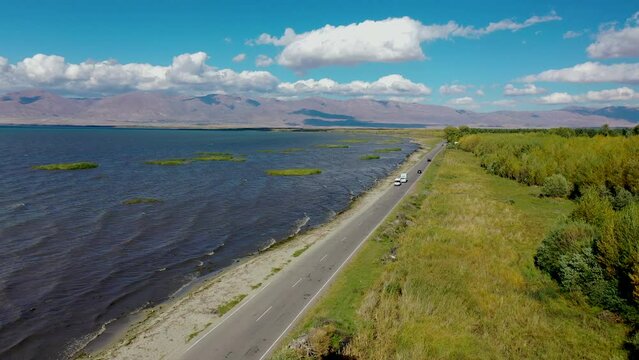 Aerial view highway traffic near water.  Road near Sevan lake in Armenia, Caucasus. Cars driving on asphalt road near lake in Armenia, western Asia. Aerial footage road between lake and field.